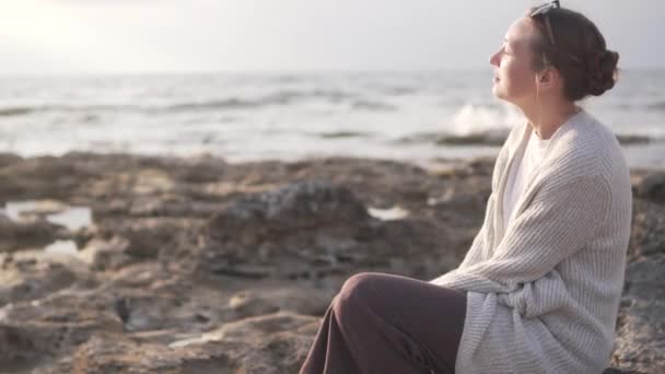 Kayalık bir sahilde oturan şık genç kadın — Stok video