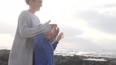 Anne ve oğlu denizde gün batımını izliyorlar.