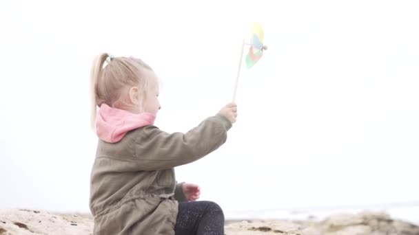 Милая маленькая девочка с ветряной мельницей на голубом фоне неба — стоковое видео