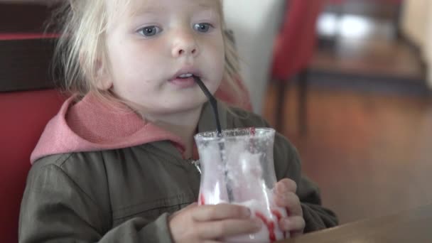 Una niña bebe un cóctel de leche de vainilla en un café — Vídeo de stock