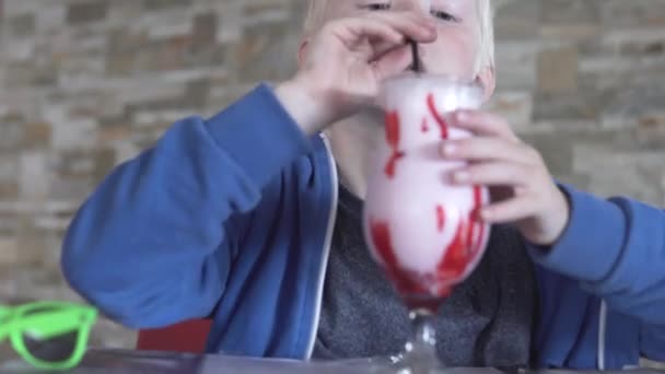 En blond pojke dricker en mjölk cocktail från en stor stack — Stockvideo