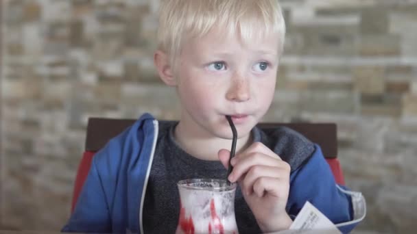 Lindo chico rubio bebiendo batido de fresa — Vídeo de stock