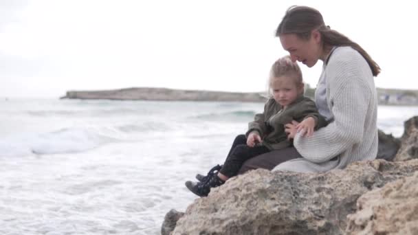 Mamma och hennes lilla dotter sitter på klipporna vid havet och pratar — Stockvideo