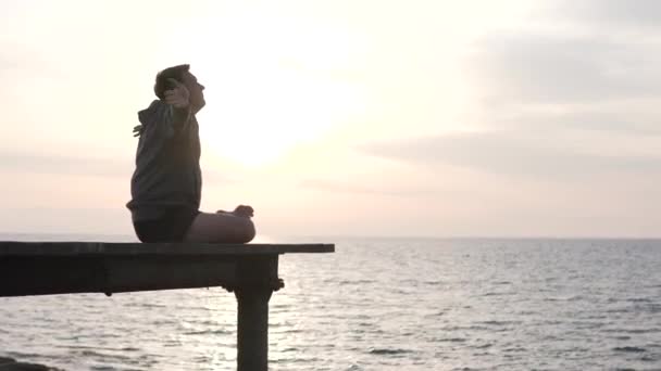 Een man beoefent yoga met een uitzicht op de zonsondergang op de zee — Stockvideo