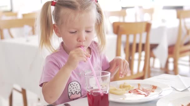 Красивая маленькая девочка ест картошку фри с кетчупом в кафе — стоковое видео