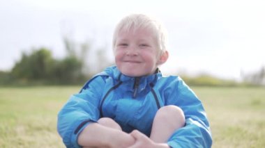Yakışıklı bir albino çocuk çim bir parkta oturan ve gülümseyen