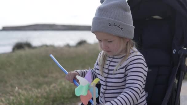 Klein meisje zittend in een kinderwagen en spelen met een speelgoed windmolen — Stockvideo