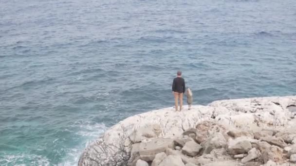 Un hombre y su hijita están parados sobre una roca blanca y mirando al océano — Vídeos de Stock