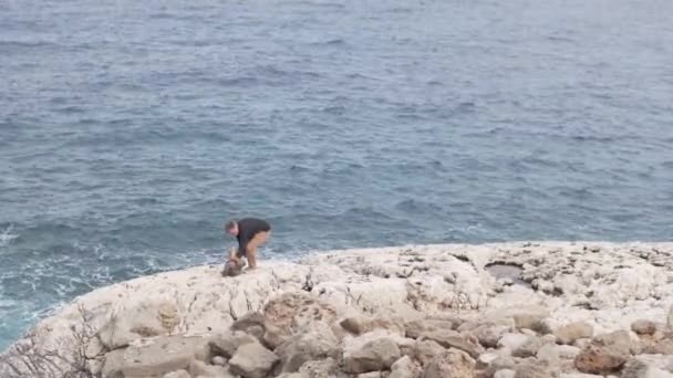 Un hombre y su hijita están parados sobre una roca blanca y mirando al océano — Vídeos de Stock