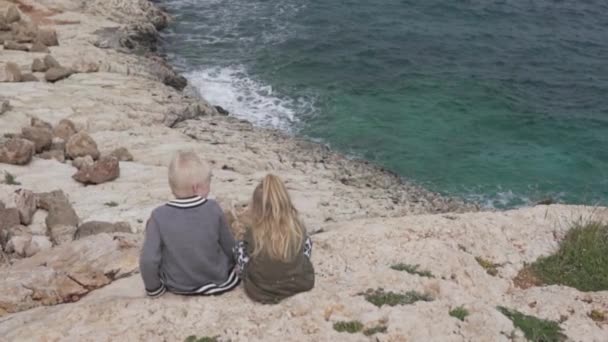 Un ragazzo e una bambina sono seduti sul bordo di una scogliera cercando — Video Stock