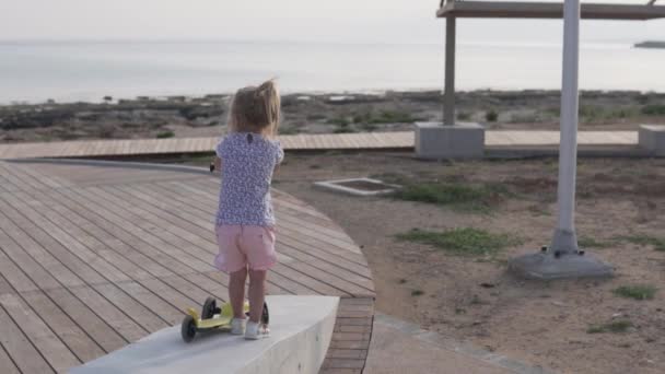 Красива маленька дівчинка катається на скутері на заході сонця — стокове відео