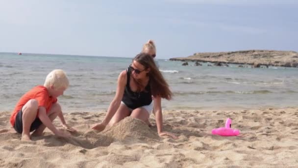 Η οικογένεια στέκεται άμμο κάστρο στην παραλία δίπλα στη θάλασσα. — Αρχείο Βίντεο