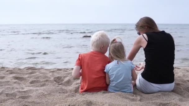 Familia con niños sentados en la playa junto al mar — Vídeo de stock