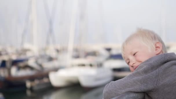 Smutny blond chłopiec stoi na molo w pobliżu jachtów i patrzy na morze — Wideo stockowe