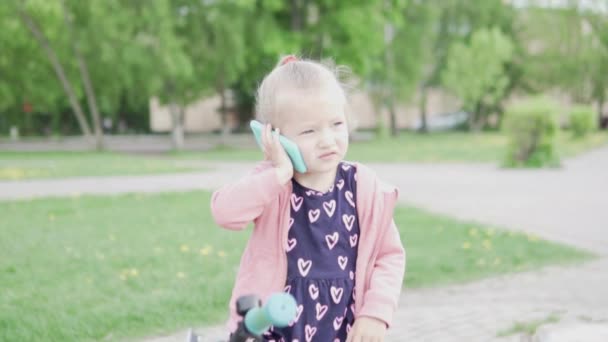 Маленькая девочка садится на велосипед и разговаривает по игрушечному телефону — стоковое видео