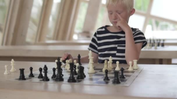 Der Junge spielt Schach. das Kind sitzt in einem geräumigen, hellen Schachclub — Stockvideo