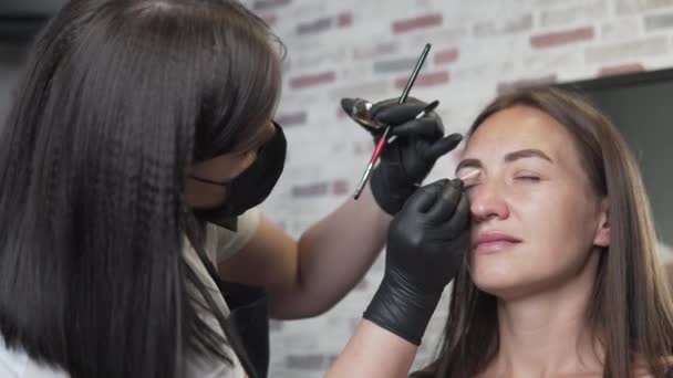 Kosmetikerin korrigiert Augenbrauen im Salon. der Augenbrauenmeister malt die Augenbrauen — Stockvideo