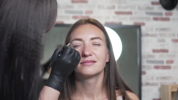 Guiden formar klientens ögonbryn. En kvinna sätter på en svart ögonbryn borste — Stockvideo