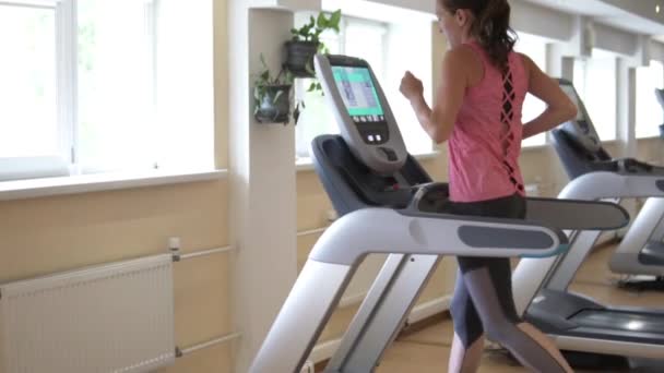 Fiatal nő fut a futópad szimulátor az edzőteremben — Stock videók