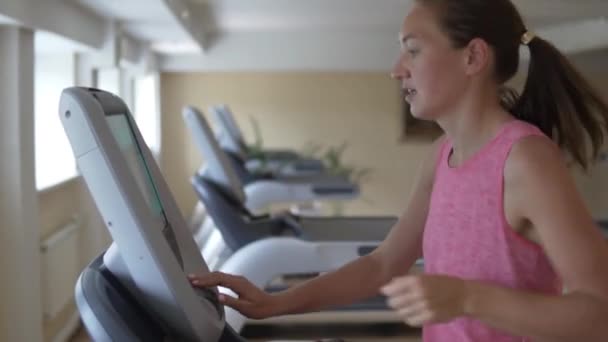 Jonge vrouw draait op de loopband simulator in de sportschool — Stockvideo
