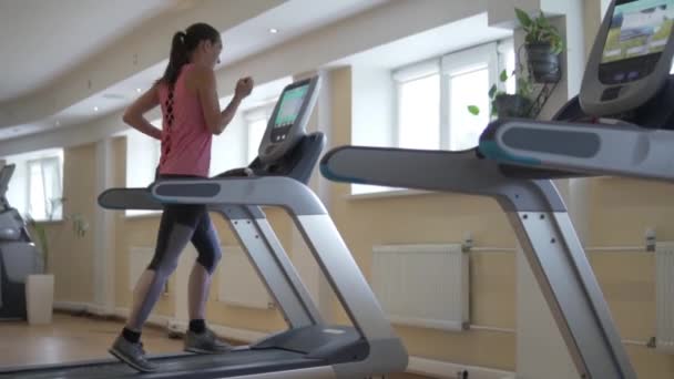 Joven mujer sexy corriendo en una cinta de correr simulador en el pasillo — Vídeos de Stock