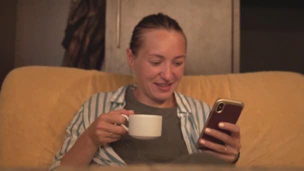 Una mujer bebe café y ve las noticias en un teléfono móvil — Vídeos de Stock