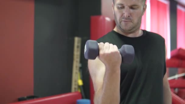 남자는 아령의 도움으로 체육관에서 자신의 근육을 흔들어 — 비디오