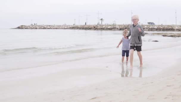 Kinder laufen am Strand am Meer entlang — Stockvideo