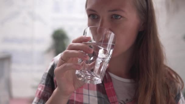 Una joven bebe agua de una taza de vidrio. — Vídeo de stock
