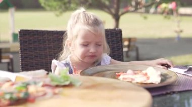 Sıcak bir yaz gününde sokakta bir kafede pizza yiyen sevimli küçük kız