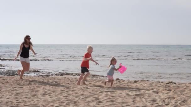 Matka z dziećmi bawiącymi się na plaży nad morzem — Wideo stockowe