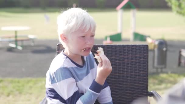 Süßer blonder Junge isst Pizza in einem Straßenrestaurant — Stockvideo