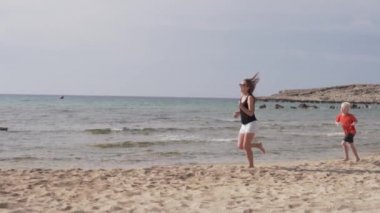 anne ve oğlu kumlu plaj boyunca koşuyor. Oğlu denizde yetişmek için anne ile oynar