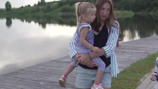 Anne ve çocuklar nehir kıyısındaki parkta yürüyorlar. — Stok video