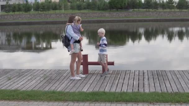 Moeder en kinderen lopen in de zomer langs de dijk van de rivier. — Stockvideo