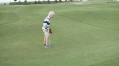Sarışın bir çocuk golf sahasında koşuşturuyor.