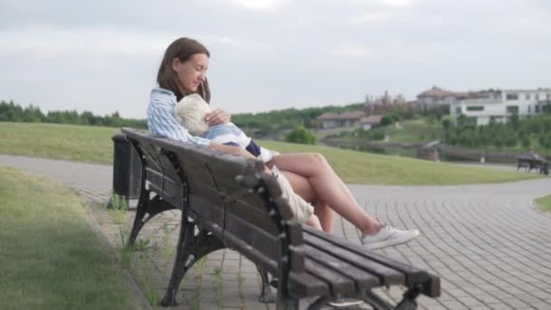 Mama i syn siedzą na ławce w parku i czekają na zachód słońca — Wideo stockowe