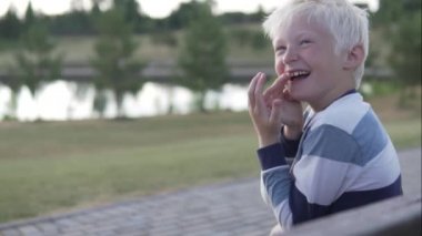 Bir albino çocuk neşeli bir şekilde gülüyor. Gülüyor ve kahkahalarla ağzını kapatıyor.