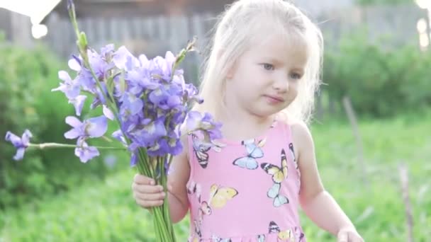 Klein meisje blonde snuift een boeket van blauwe irissen. — Stockvideo