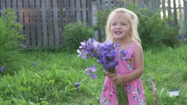 Schönes kleines Mädchen hält einen Strauß blauer Blumen in der Hand und lacht — Stockvideo