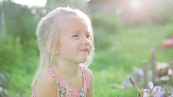 Mooi klein meisje met een boeket van blauwe klokken staat in de tuin. — Stockvideo