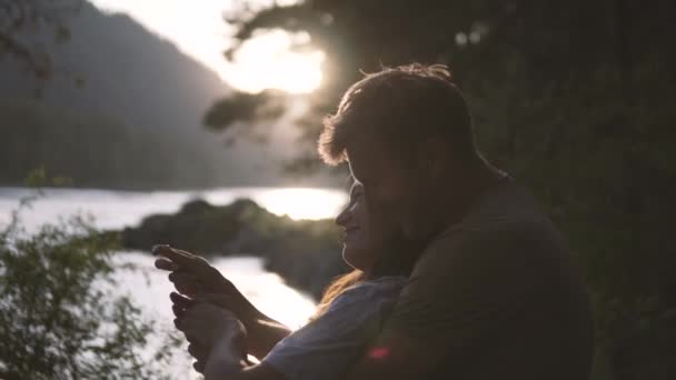 Ett kärleksfullt par som tittar på solnedgången vid en fjäll flod. — Stockvideo