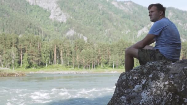 Σοβαρός στοχαστικός άνθρωπος κοιτάζει σε ένα ορεινό ποτάμι. — Αρχείο Βίντεο