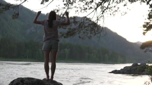 Kvinna dansar på en sten vid solnedgången av en fjäll flod. — Stockvideo