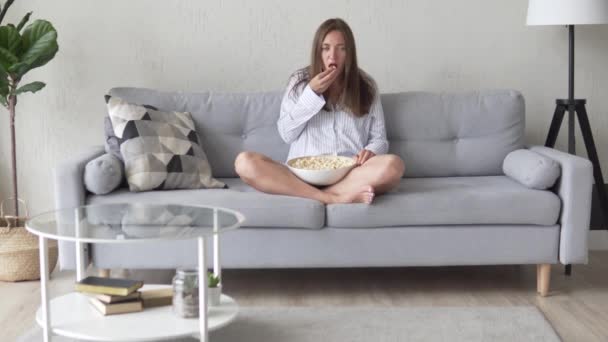 Молодая женщина смотрит телевизор и ест попкорн — стоковое видео