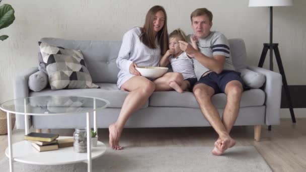 Familia viendo televisión en casa y comiendo palomitas de maíz — Vídeo de stock