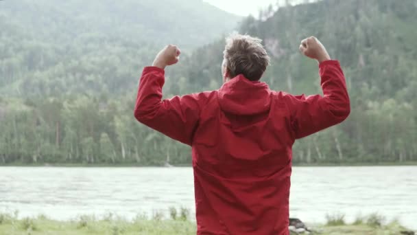 Un uomo alza felicemente le mani alla fine di un difficile percorso escursionistico . — Video Stock