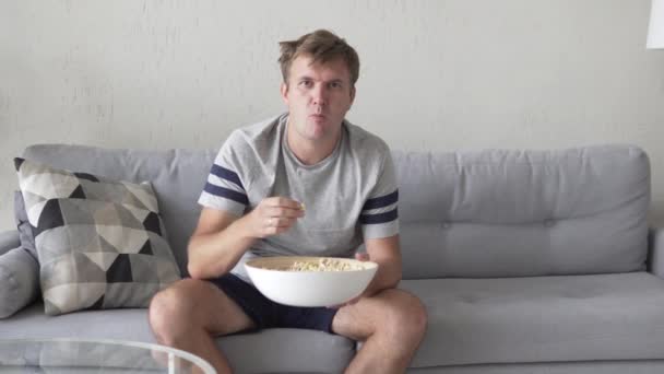 Een man kijkt TV en eet popcorn — Stockvideo