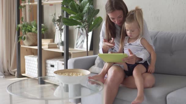 Mamá y su hija juegan un juego educativo en una tableta en casa . — Vídeo de stock