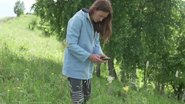 Eine Frau fotografiert Blumen auf einem Feld mit ihrem Handy. — Stockvideo